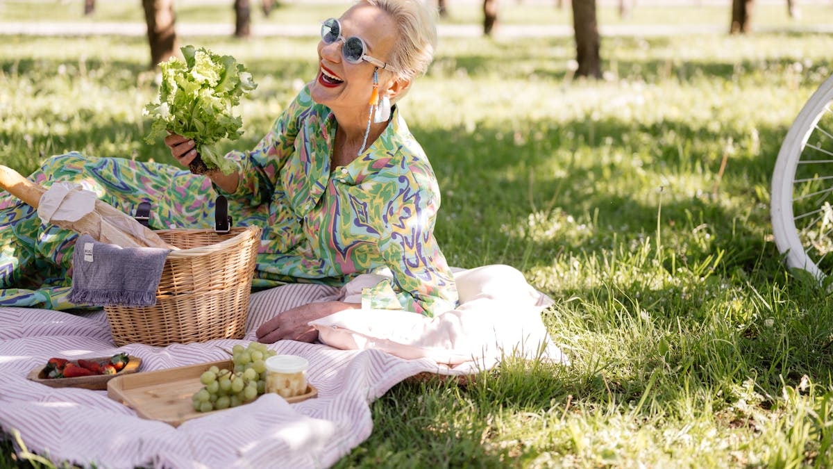 Elderly woman enjoying a picnic with vibrant clothing and fresh greenery.