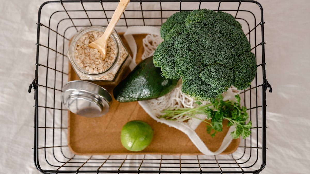 A flat lay of fresh, healthy ingredients including broccoli, avocado, lime, and oats in a basket.